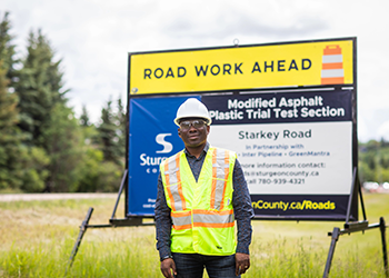 a person wearing a safety vest and hard hat standing in front of a sign