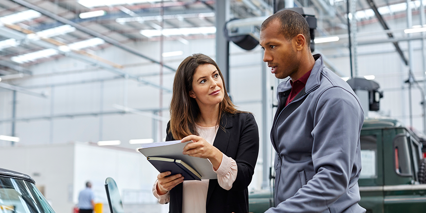 Three people are discussing and examining a piece of machinery in an industrial workshop. One person is explaining, another is holding a tablet, and the third is observing thoughtfully.