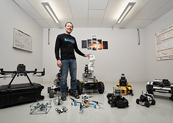 A man stands in front of numerous robots in a room