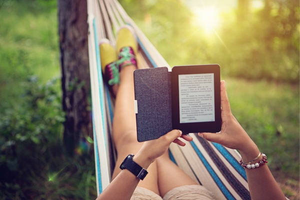 A woman, in a hammock, reading a book on her Kindle, focused and relaxed in a cozy outdoor setting.