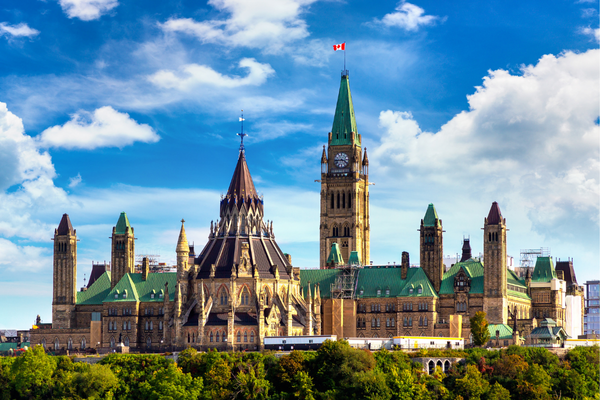 The Canadian Parliament Buildings in Ottawa, featuring green copper roofs, gothic architecture, and a tall central clock tower with the Canadian flag.