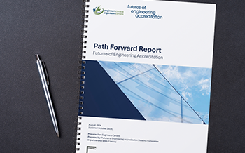 A spiral-bound document titled "Path Forward Report: Futures of Engineering Accreditation" by Engineers Canada, lying on a dark surface next to a silver pen.