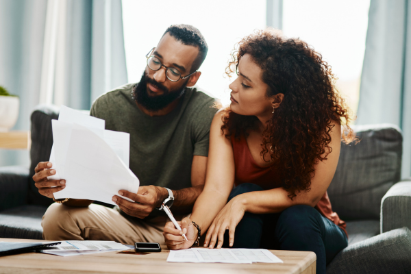 A couple sitting on a sofa reviewing and signing financial documents together at a coffee table.