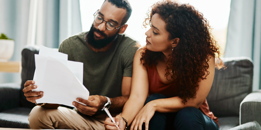 Un couple assis sur un canapé examine et signe des documents financiers sur une table basse.