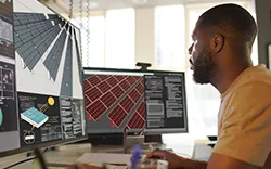 L'image montre une personne travaillant devant plusieurs écrans d'ordinateur affichant divers types de données et d'interfaces.