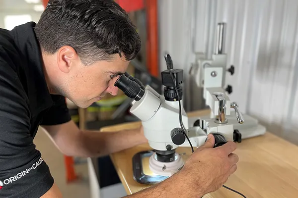 Une personne en chemise noire mène une expérience de microscopie, en ajustant la mise au point sur un microscope blanc placé sur un bureau en bois, avec un autre microscope à l'arrière-plan.