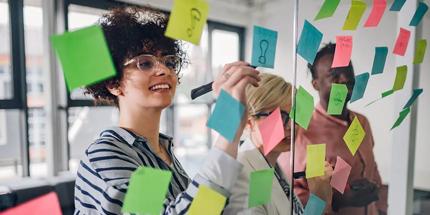 A group of people looking at a glass wall covered with a variety of coloured sticky notes