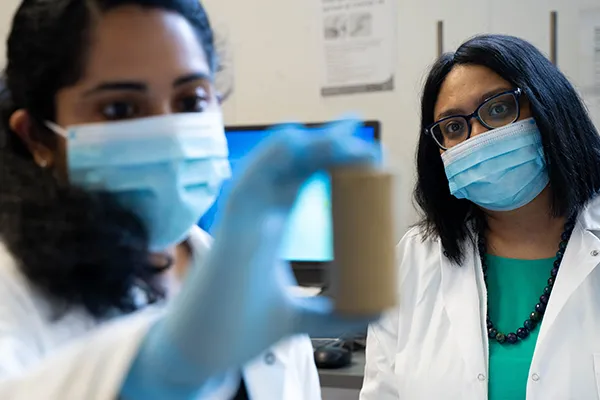 Deux scientifiques portant des masques et des blouses examinent un échantillon dans un laboratoire.