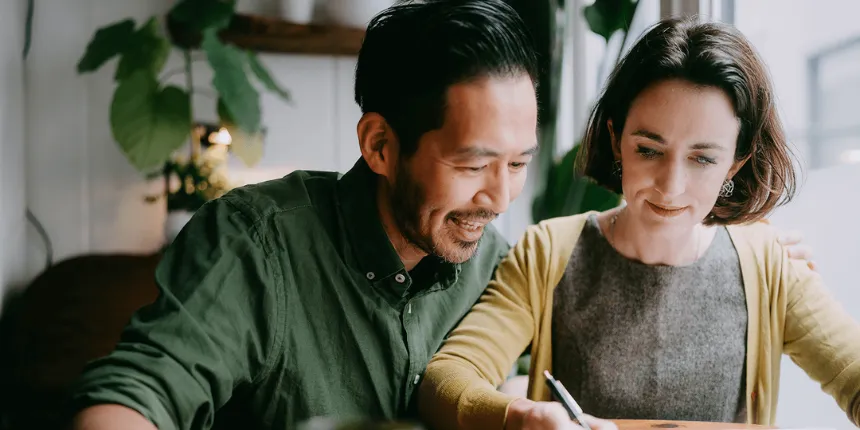 Un homme et une femme sont assis côte à côte à une table, souriants, concentrés sur ce qu'ils écrivent dans un cahier.