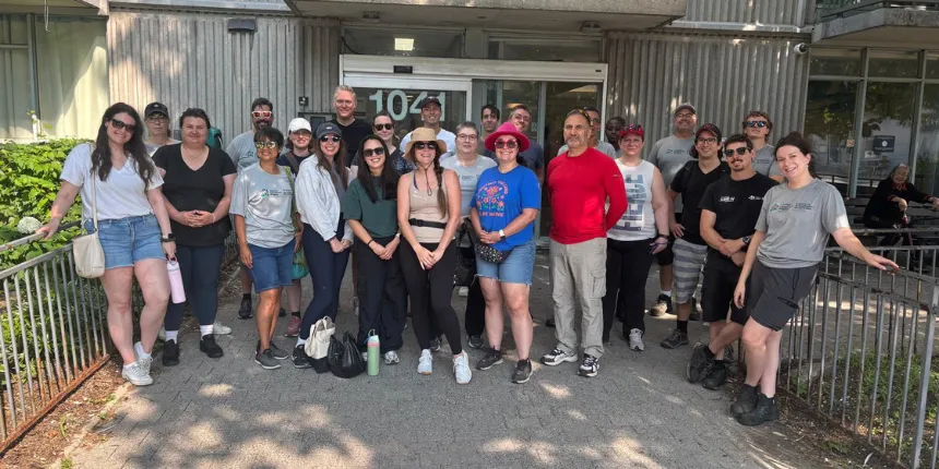 Photo de groupe montrant des bénévoles d’Ingénieurs Canada posant devant l’entrée d’un immeuble de logement communautaire. Le groupe compte environ deux douzaines de personnes vêtues de tenues de travail décontractées, qui sourient à l’appareil photo à l’extérieur par une journée ensoleillée.