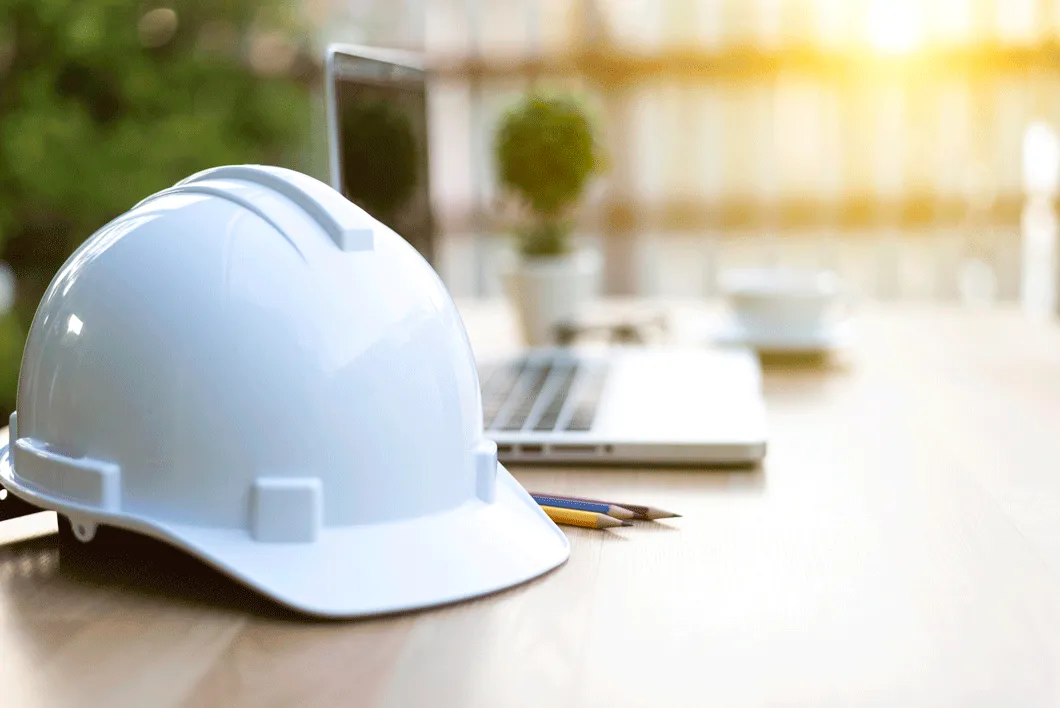 White hardhat on a desk beside a laptop
